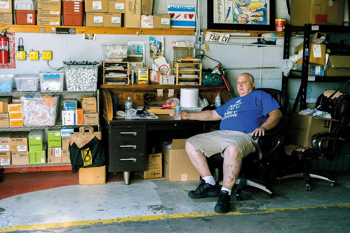 John Gunterson, sentado en el garaje en el que se guardan las camionetas de intercambio de jeringuillas de la Chicago Recovery Alliance. Gunterson,  lleva puesta una camiseta con el lema “Keep calm and carry naloxone” diseñada por el propio Nigel Brunsdon.